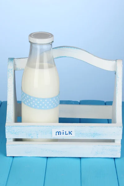 Milch in Flasche in Holzkiste auf blauem Holztisch auf blauem Hintergrund — Stockfoto