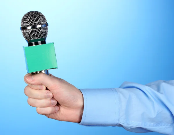 Male hand with microphone on blue background — Stock Photo, Image