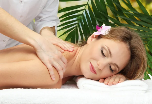 Hermosa mujer en el salón de spa recibiendo masaje, en el fondo de hojas de palma —  Fotos de Stock