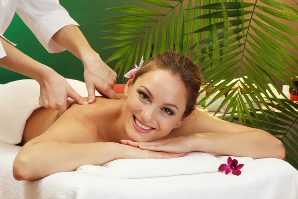 Hermosa mujer en el salón de spa con piedras recibiendo masaje, sobre fondo verde —  Fotos de Stock