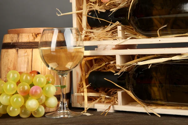 Cassa in legno con bottiglia di vino, botte, bicchiere da vino e uva su tavolo in legno su sfondo grigio — Foto Stock