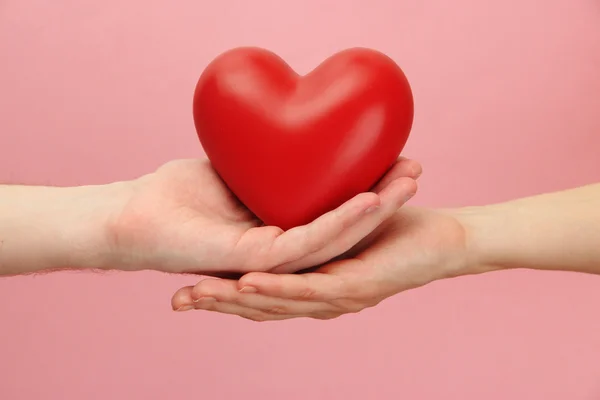 Красное сердце в руках женщины и мужчины, на розовом фоне — стоковое фото
