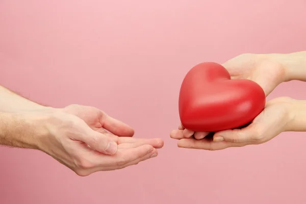 Corazón rojo en manos de hombre y mujer, sobre fondo rosa — Foto de Stock
