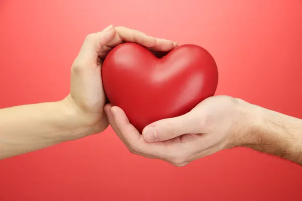 Corazón rojo en manos de hombre y mujer, sobre fondo rojo — Foto de Stock