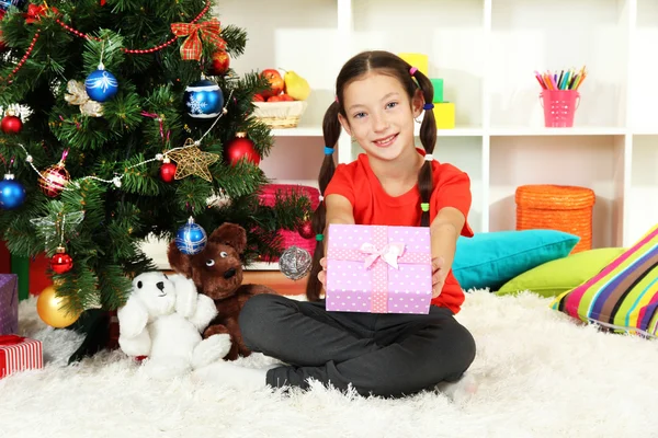 Little girl holding gift box near christmas tree — Stock Photo, Image