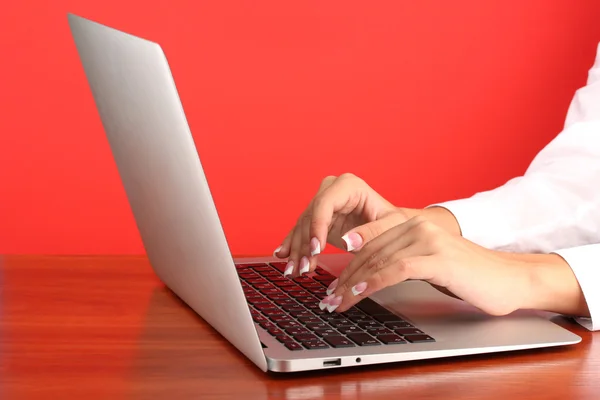 Mãos de mulher de negócios digitando no computador portátil, no fundo vermelho close-up — Fotografia de Stock