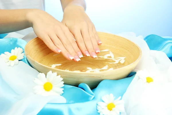 Donna mani con ciotola di legno di acqua con fiori, su sfondo blu — Foto Stock