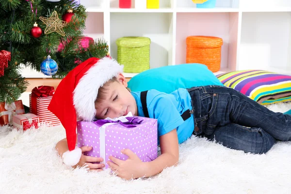 Μικρό αγόρι έπεσε κοιμισμένος με δώρο στα χέρια του κάτω από το χριστουγεννιάτικο δέντρο που περιμένουν τον Άγιο Βασίλη να έρθει — Φωτογραφία Αρχείου
