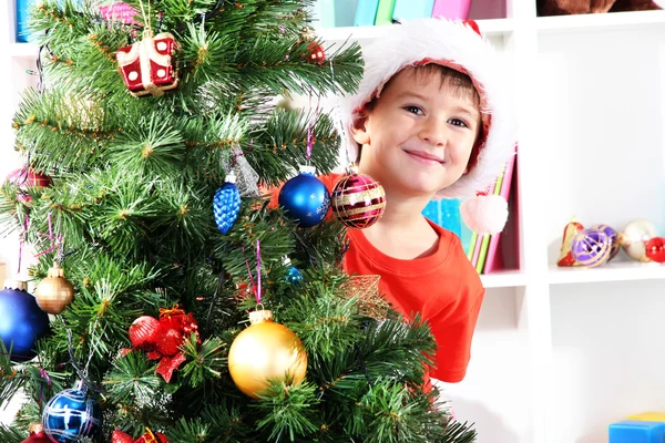 Niño en el sombrero de Santa mira hacia fuera desde detrás del árbol de Navidad —  Fotos de Stock