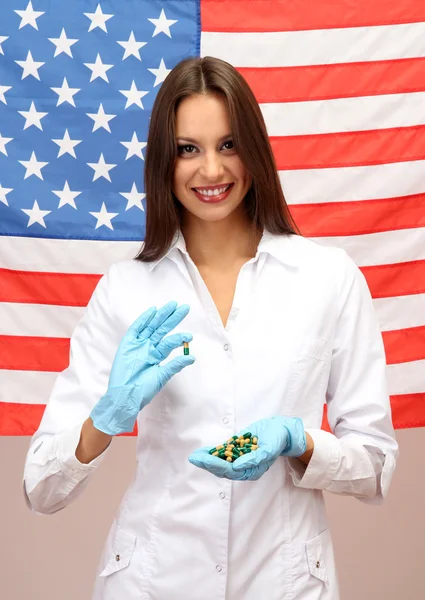 Портрет женщины-врача или ученого, показывающий и анализирующий таблетки на фоне американского флага — стоковое фото