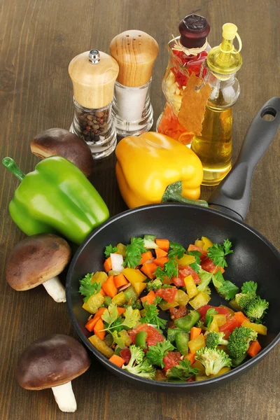 Hortalizas frescas en rodajas en sartén con especias e ingredientes sobre mesa de madera — Foto de Stock