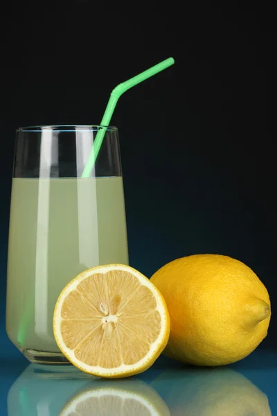 Delicioso zumo de limón en vaso y limones al lado sobre fondo azul oscuro — Foto de Stock