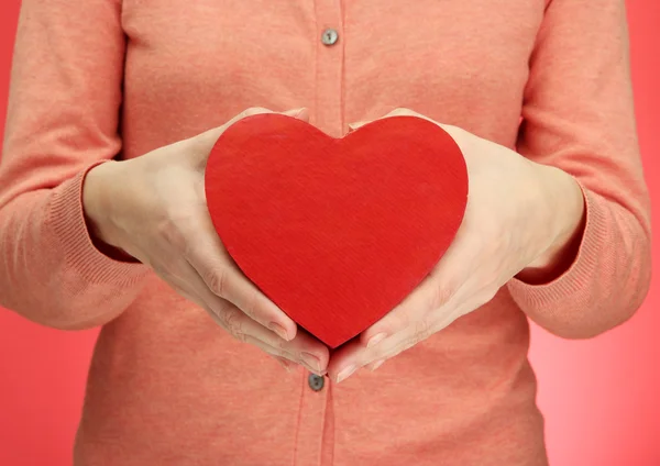 Coeur rouge dans les mains de la femme, sur fond rouge — Photo