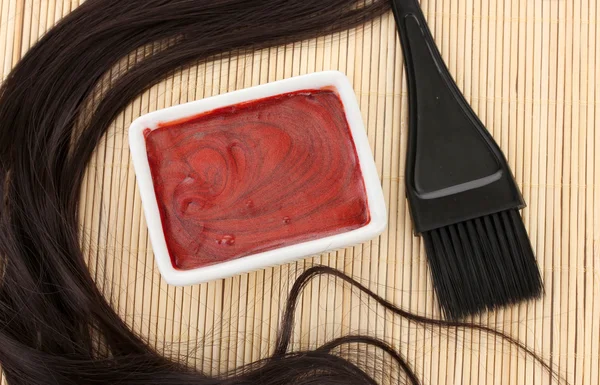 Hair dye in bowl and brush for hair coloring on beige bamboo mat, close-up Stock Photo