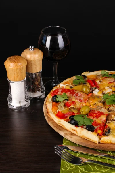 Pyszne pizze z kieliszek czerwonego wina i przyprawy na drewnianym stole na czarnym tle — Zdjęcie stockowe