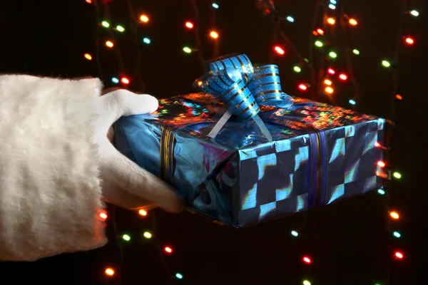 Santa Claus hand holding gift box on bright background — Stock Photo, Image