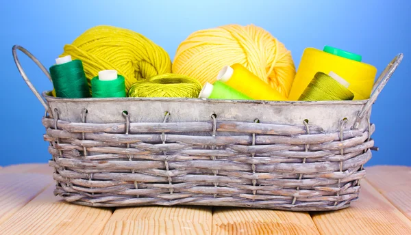 Bright threads in basket on wooden table on blue background — Stock Photo, Image