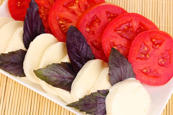 Schmackhafter Mozzarella mit Tomaten auf Teller auf Matte — Stockfoto