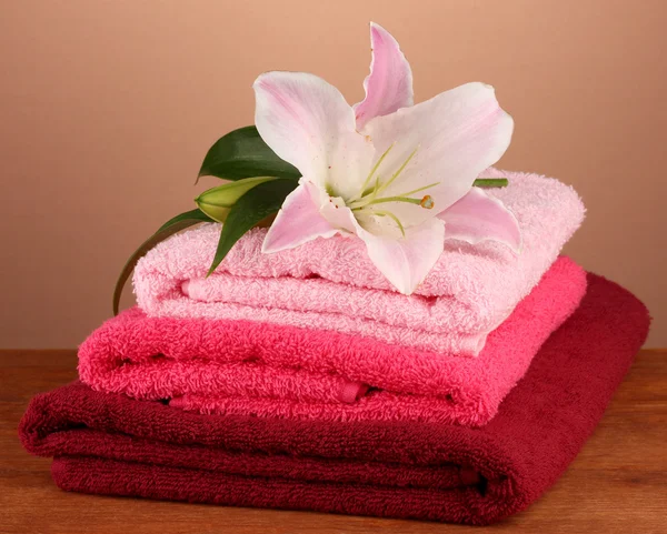 Στοίβα πετσέτες με ροζ κρίνος σε καφέ φόντο — Φωτογραφία Αρχείου