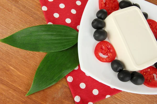 Feta cheese on plate decorated with olives and tomatoes on wooden table close-up — Stock Photo, Image