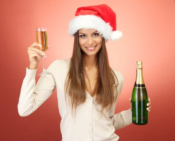 Beautiful young woman with bottle and glass of champagne, on red background — Stock Photo, Image
