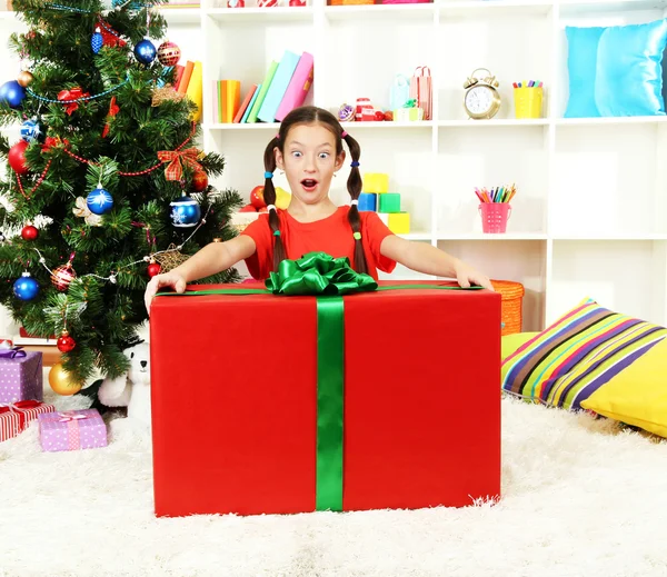 Little girl with large gift box near christmas tree — Stock Photo, Image