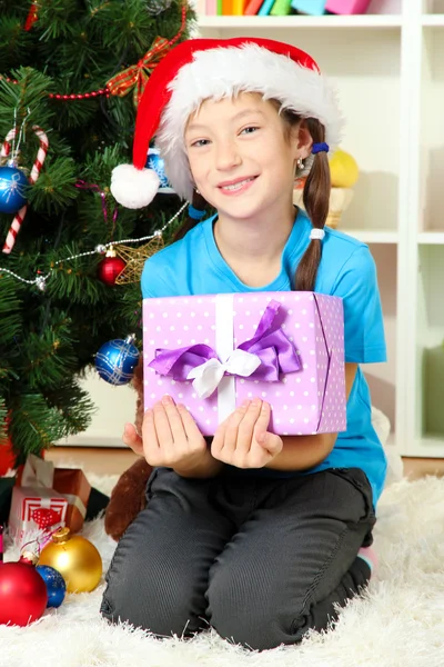 Klein meisje houden de doos van de gift in de buurt van de kerstboom — Stockfoto