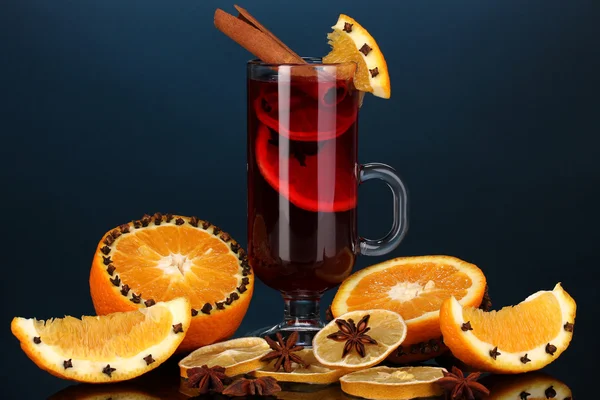 Fragrant mulled wine in glass with spices and oranges around on blue background — Stock Photo, Image