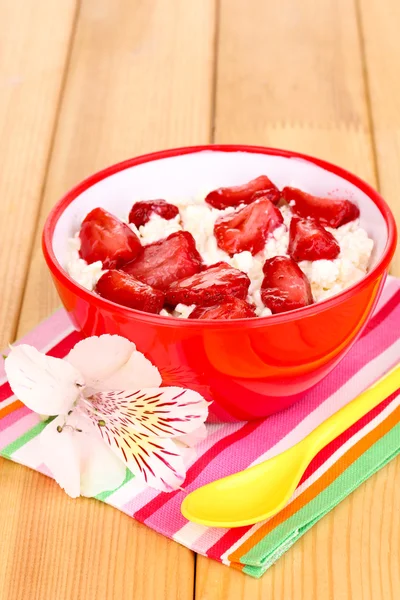 Hüttenkäse in roter Schüssel mit Erdbeeren in Scheiben auf Holztisch — Stockfoto