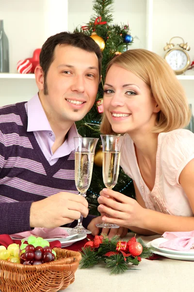 Młoda szczęśliwa para trzyma okulary z szampanem przy stole w pobliżu choinki — Zdjęcie stockowe