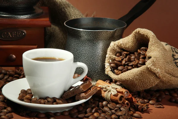 Kopp kaffe, kvarn, turk och kaffebönor på brun bakgrund — Stockfoto