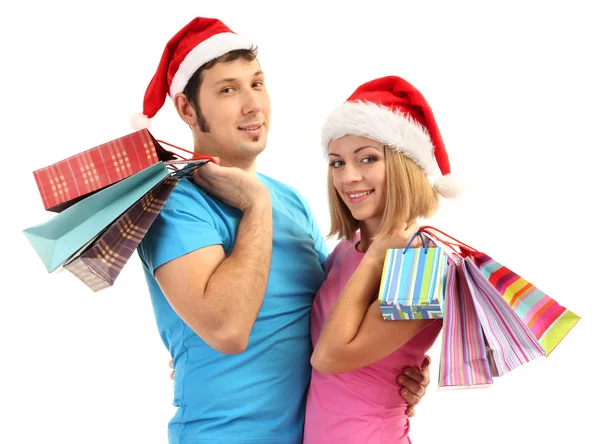 Genç bir çift olarak alışveriş ve birçok alışveriş torbaları üzerinde beyaz izole holding santa şapkalar — Stok fotoğraf