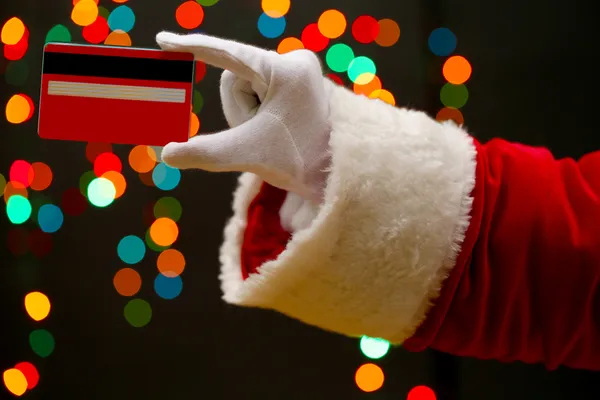 Santa Claus mano celebración de la tarjeta de crédito, sobre fondo de guirnalda — Foto de Stock