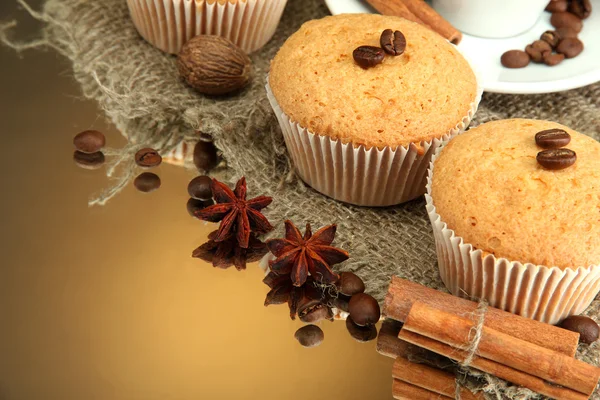 Tasty muffin cakes with spices on burlap and cup of coffee, on brown background — Stock Photo, Image