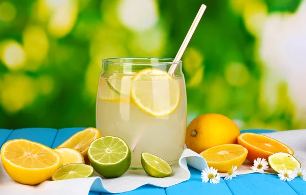 Citrus lemonade in glass bank of citrus around on blue wooden table on natural background — Stock Photo, Image