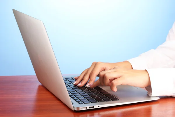 Mani di donna d'affari digitando sul computer portatile, su sfondo blu primo piano — Foto Stock