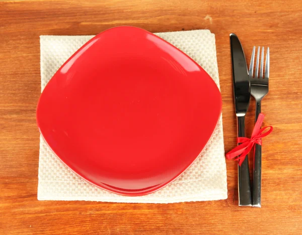 Empty square red plate with fork and knife on wooden table, close-up — Stock Photo, Image