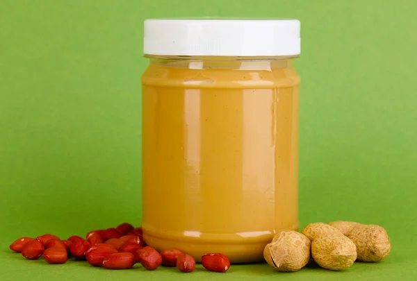 Смачне арахісове масло в банці з арахісом поблизу на зеленому фоні — стокове фото