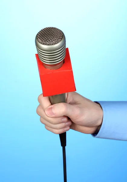 Mano masculina con micrófono sobre fondo azul — Foto de Stock