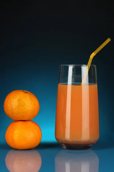 Utsökt tangerine juice i glas och mandariner bredvid den på Mörkblå bakgrund — Stockfoto