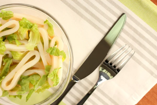 Salad of squid rings, lemon and lettuce in a glass bowl on striped tablecloth close-up — Stock Photo, Image