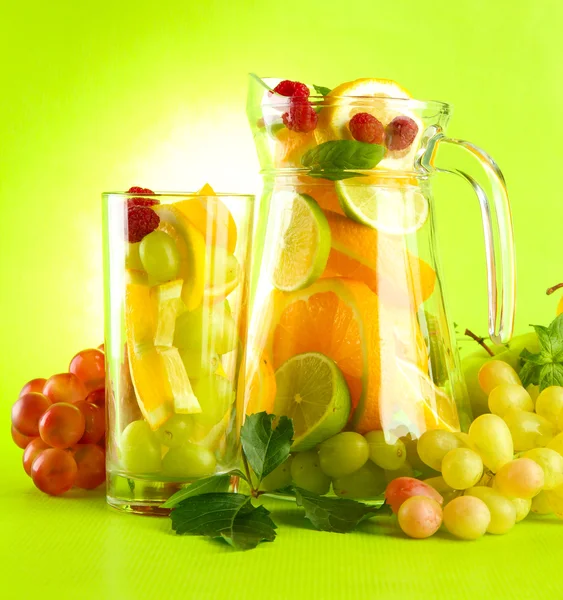 Jar and glass with citrus fruits and raspberries, on green background — Stock Photo, Image