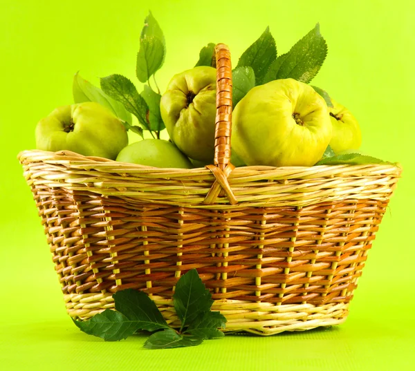 Sweet quinces with leaves in basket, on green background — Stock Photo, Image