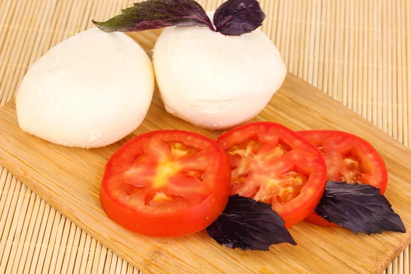 Smakelijke mozzarella met tomaten op het bord hakken op mat — Stockfoto