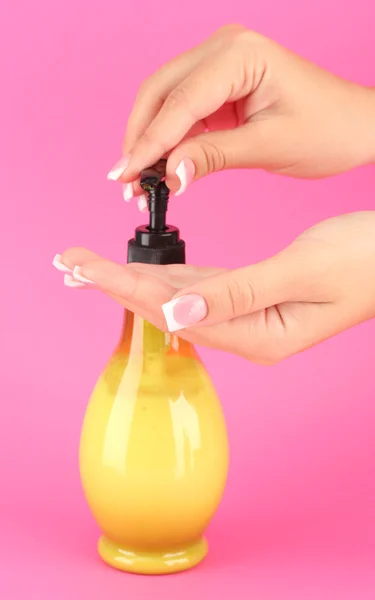 Mujer apretando loción en su mano, sobre fondo rosa de cerca — Foto de Stock