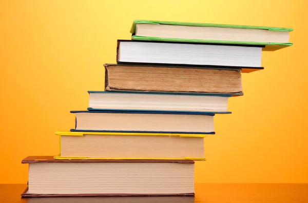 Stapel interessanter Bücher und Zeitschriften auf Holztisch auf orangefarbenem Hintergrund — Stockfoto