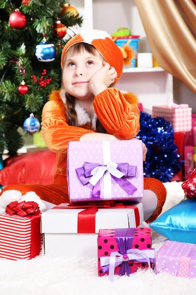 Dreaming little girl in suit of squirrels surrounded by gifts in festively decorated room — Stock Photo, Image