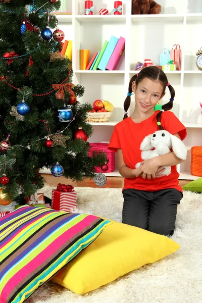 Menina segurando brinquedo perto da árvore de natal — Fotografia de Stock