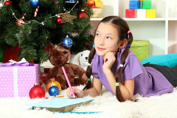 Liten flicka skriva brev till santa nära julgran — Stockfoto