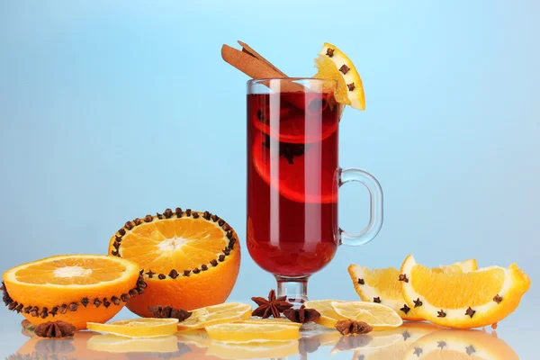 Fragrant mulled wine in glass with spices and oranges around on blue background — Stock Photo, Image